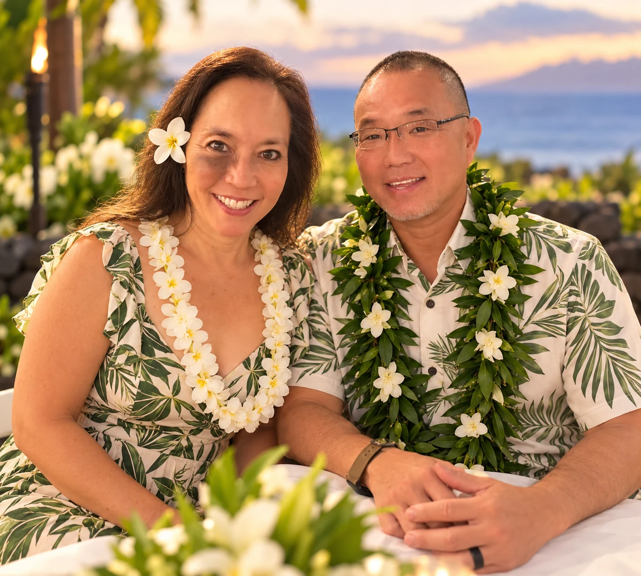 Two people wearing flower leis beside the ocean at sunset